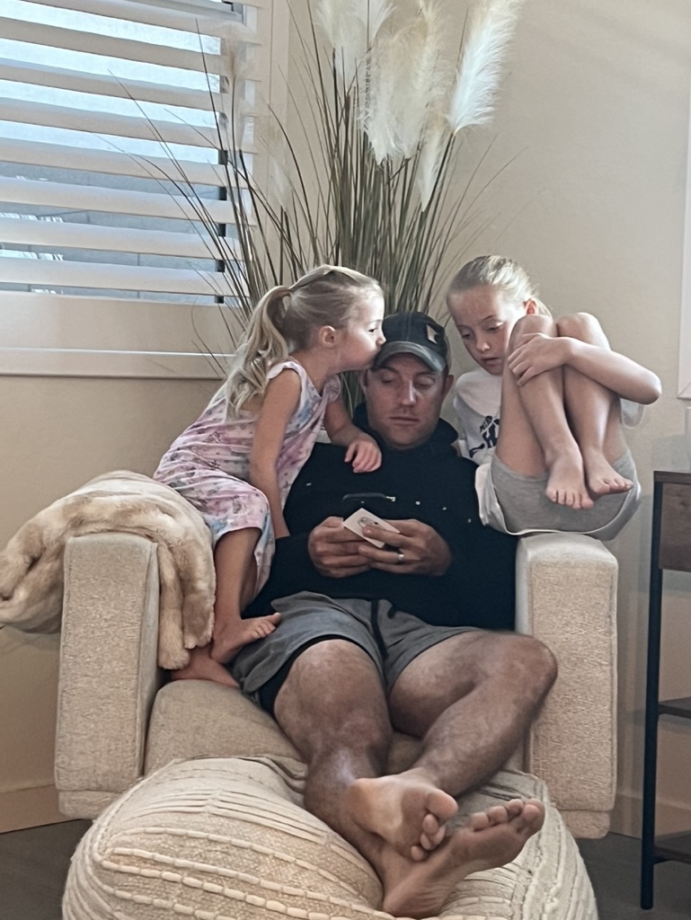 Both daughters curled up next to Brian on a chair — one kissing his cheek — while he looks at his phone